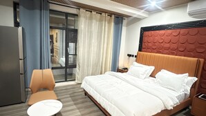 Une chambre d’hôtel comprenant un lit, une chaise, un bureau, un réfrigérateur et une porte-fenêtre coulissante donnant sur un balcon.