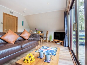 Ein Wohnzimmer mit einem braunen Ledersofa, einem Couchtisch mit einem Gesellschaftsspiel und einem Fernseher im Hintergrund.
