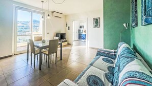 Una sala de estar con sofá, mesa de comedor, sillas y televisor. Se observa una cocina al fondo.