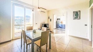 Un comedor con una mesa y sillas de vidrio, una cocina al fondo y vistas a través de un puerta corredera.