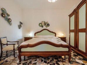 Ein Schlafzimmer mit einem hölzernen Bett, einem Sessel, einem Nachttisch, einem Kleiderschrank und Wanddekoration.