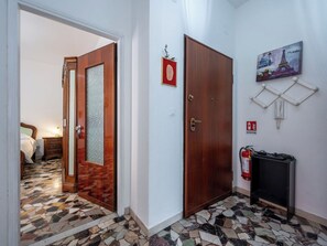 Ein Flur mit Mosaikboden, einer Holztür, einem Bett im angrenzenden Zimmer und einem Feuerlöscher an der Wand.