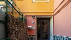 Un muro de piedra, una barandilla de metal, una puerta con un número y una planta en maceta.