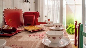 Un área de comedor con una mesa preparada para dos personas, que incluye pizza, una tetera, tazas y una silla roja.