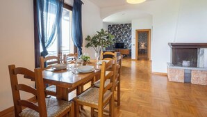 Een eetruimte met een houten tafel en stoelen, een plant in een pot en een televisie op de achtergrond.