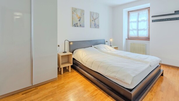 Et moderne soveværelse med en seng, sengeborde, lamper, en radiator og to billeder hængt på væggen.