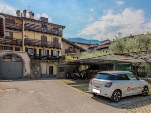 Ein weißes Auto vor einem Gebäude mit Garage und überdachtem Parkplatz, im Hintergrund Berge.