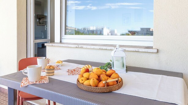 A table with a basket of fruit, a mug, and a candle on a balcony with a city view. - Lovely apartment for 4 people with WIFI, A/C, TV, balcony and panoramic view (Lido Di Fermo)
