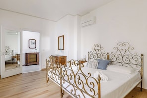 Ein Schlafzimmer mit einem Metallbettgestell, einer Holzkommode, einem Spiegel und einem Bild an der Wand.