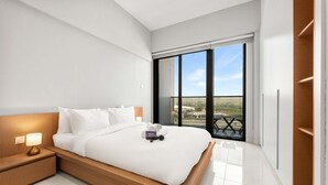 A modern bedroom with a large bed, a nightstand with a lamp, and a view of the outdoors through a sliding door. - Free Housekeeping Visits During Your Stay - Stayshort - Studio in Dubai Land That Sleeps 3 Close to Global Village (Dubai)