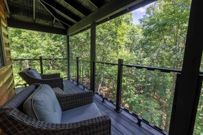 A covered porch with wicker furniture and a view of a forest. - Sky's the Limit - Make a Wish Come True and Book a Treehouse (Cleveland)