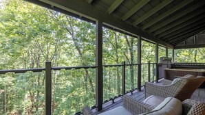Un espace extérieur aménagé, abrité et doté de meubles en osier, offrant une vue sur une forêt.