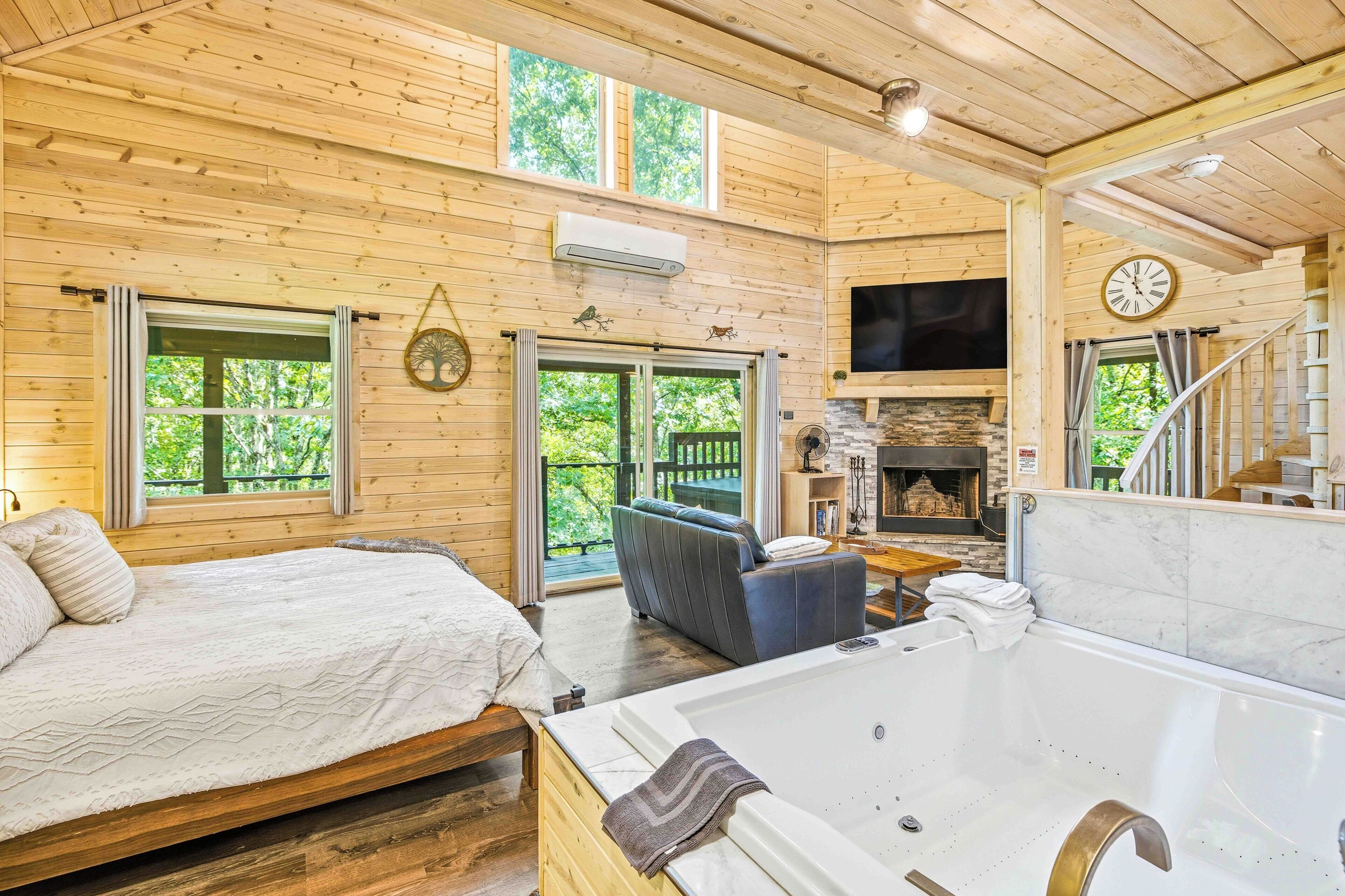 A wooden cabin interior with a bed, a sofa, a fireplace, and a large window.