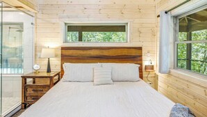 Une chambre à coucher dans une cabane en bois, avec un lit, des tables de chevet, une fenêtre et une vue sur les arbres.