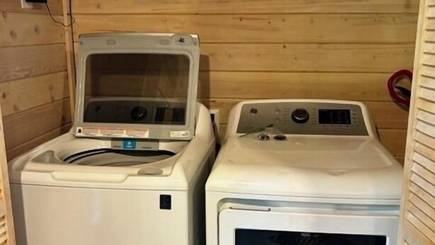 Une buanderie avec deux machines à laver blanches et un sèche-linge, des murs en bois et une étagère au-dessus des machines.