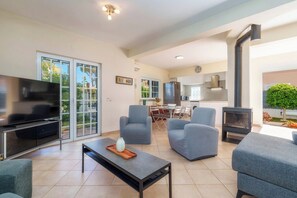 A living room with a TV, sofas, a coffee table, and a fireplace. - 3-Bedroom Villa in Vilamoura with A/C and Wi-Fi, 10 Minutes from the Marina and Golf Course, with a Pool (Quarteira)