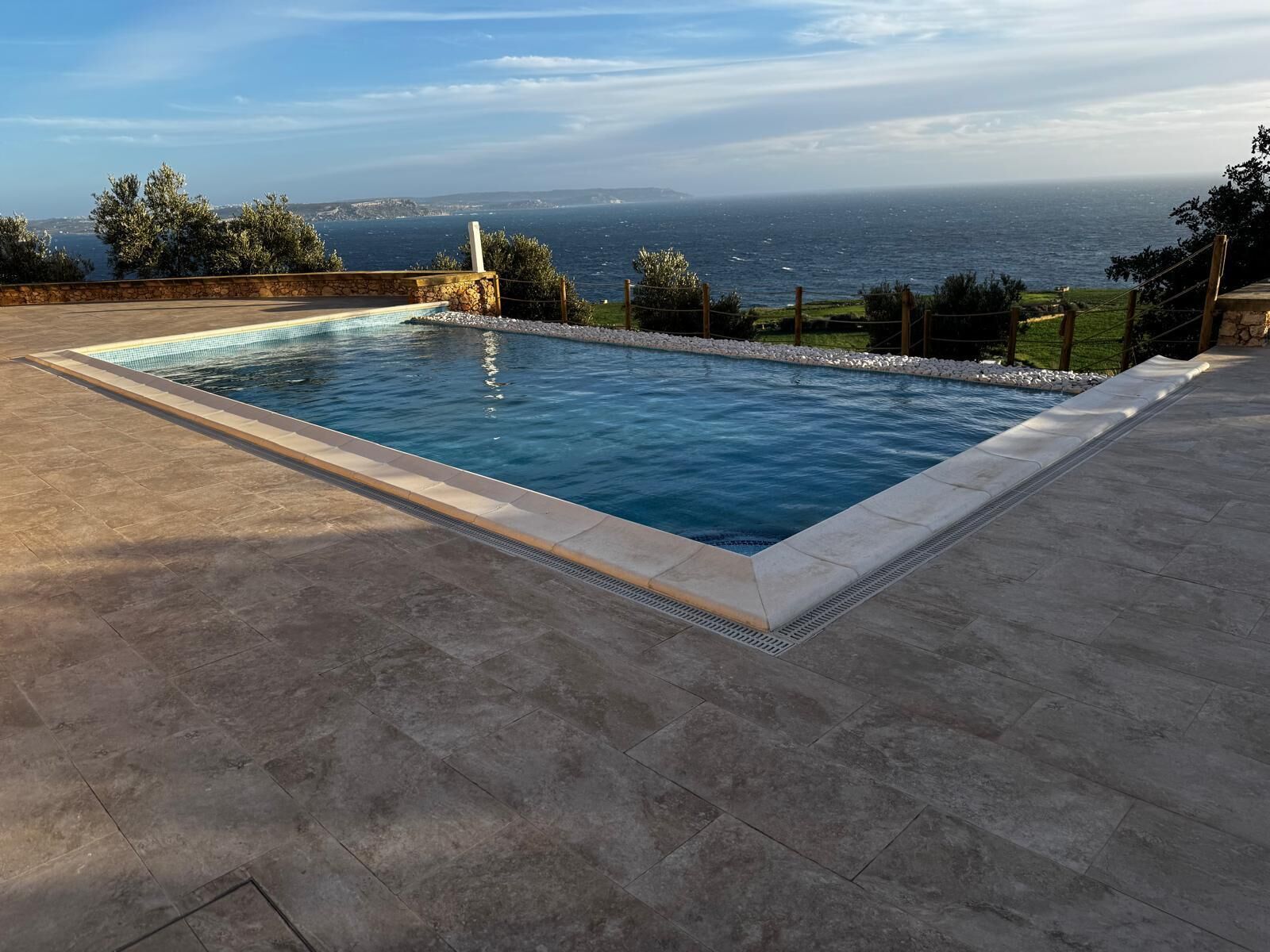 A rectangular swimming pool with a stone border, surrounded by a paved deck.