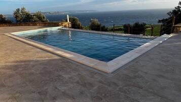 A rectangular swimming pool with a stone border, surrounded by a paved deck.