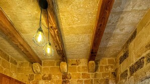 Una habitación con pared de piedra, cama de madera y lámpara colgante.