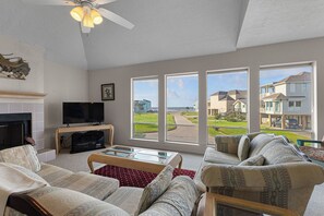 Ein Wohnzimmer mit Kamin, Fernseher und großen Fenstern mit Blick auf eine Wohngegend.