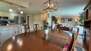 Una cocina amplia con armarios blancos, una mesa de comedor de madera y lámparas colgantes.