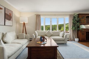 Ein Wohnzimmer mit einer Couch, einem Couchtisch und Blick auf einen Wald durch große Fenster.