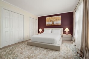 Ein Schlafzimmer mit einem Bett, zwei Nachttischen, einem Schreibtisch und einem Bild an der Wand sowie einer Tür.
