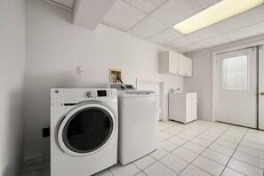 Une buanderie équipée d’un lave-linge et d’un sèche-linge à chargement frontal, d’un meuble de rangement au-dessus du sèche-linge et d’une porte avec une fenêtre.
