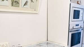 Una cocina moderna con armarios blancos, encimera de mármol, horno integrado e ilustraciones de pájaros en la pared.