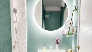 Un baño con lavamanos blanco, espejo, ducha y toallero.