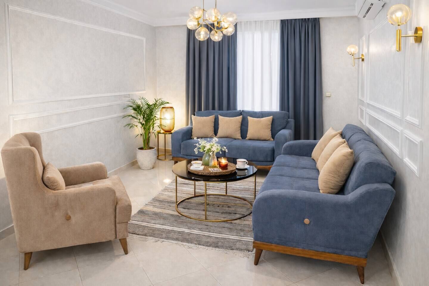 A modern living room with a beige armchair, a blue sofa set, a round coffee table, and a potted plant.