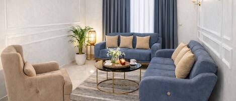 A modern living room with a beige armchair, a blue sofa set, a round coffee table, and a potted plant.