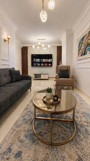 Una sala de estar con sofá, sillón, mesa de centro, televisor y obra de arte en la pared.