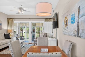 A well-lit room with a ceiling fan, a dining table with chairs, a sofa, and a television mounted on the wall. - Easy Breezy on the 16th Green in Sunset Beach (Sunset Beach)