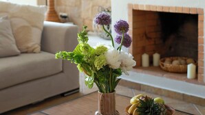 Ein Wohnzimmer mit einer Steinwand, einem runden gewebten Wandkunstwerk, einer Vase mit Blumen und Früchten sowie einem Kamin.