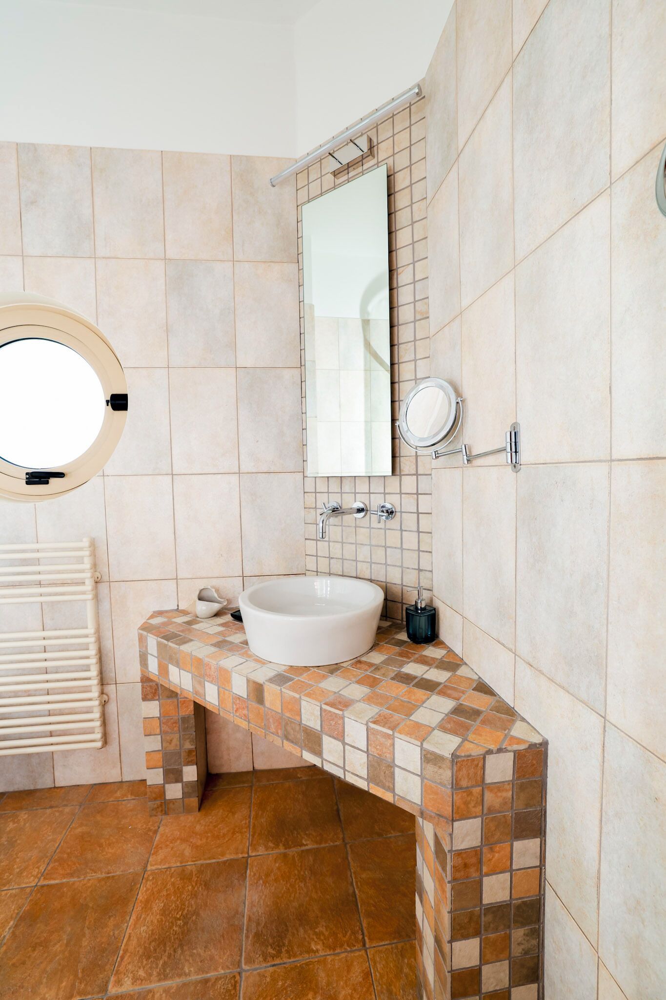 A bathroom with a white sink, a round mirror, and a tiled floor.