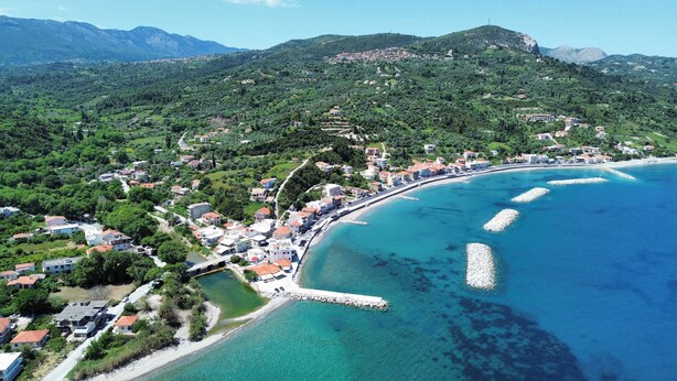 Luftaufnahme einer Küstenstadt mit Häusern, einem Strand und Bergen im Hintergrund.