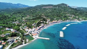 Vista aérea de un pueblo costero con casas, una playa y montañas al fondo.
