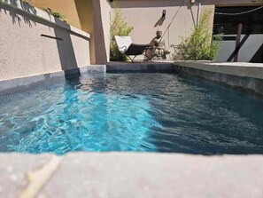 A swimming pool with clear water, a lounge chair, and a statue in the background. - le relais du luberon (Maubec)