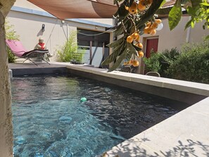 A swimming pool with clear water, surrounded by a patio area with a chair and a small statue. - le relais du luberon (Maubec)