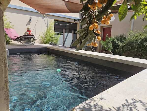 A swimming pool with clear water, surrounded by a patio area with a chair and a small statue.