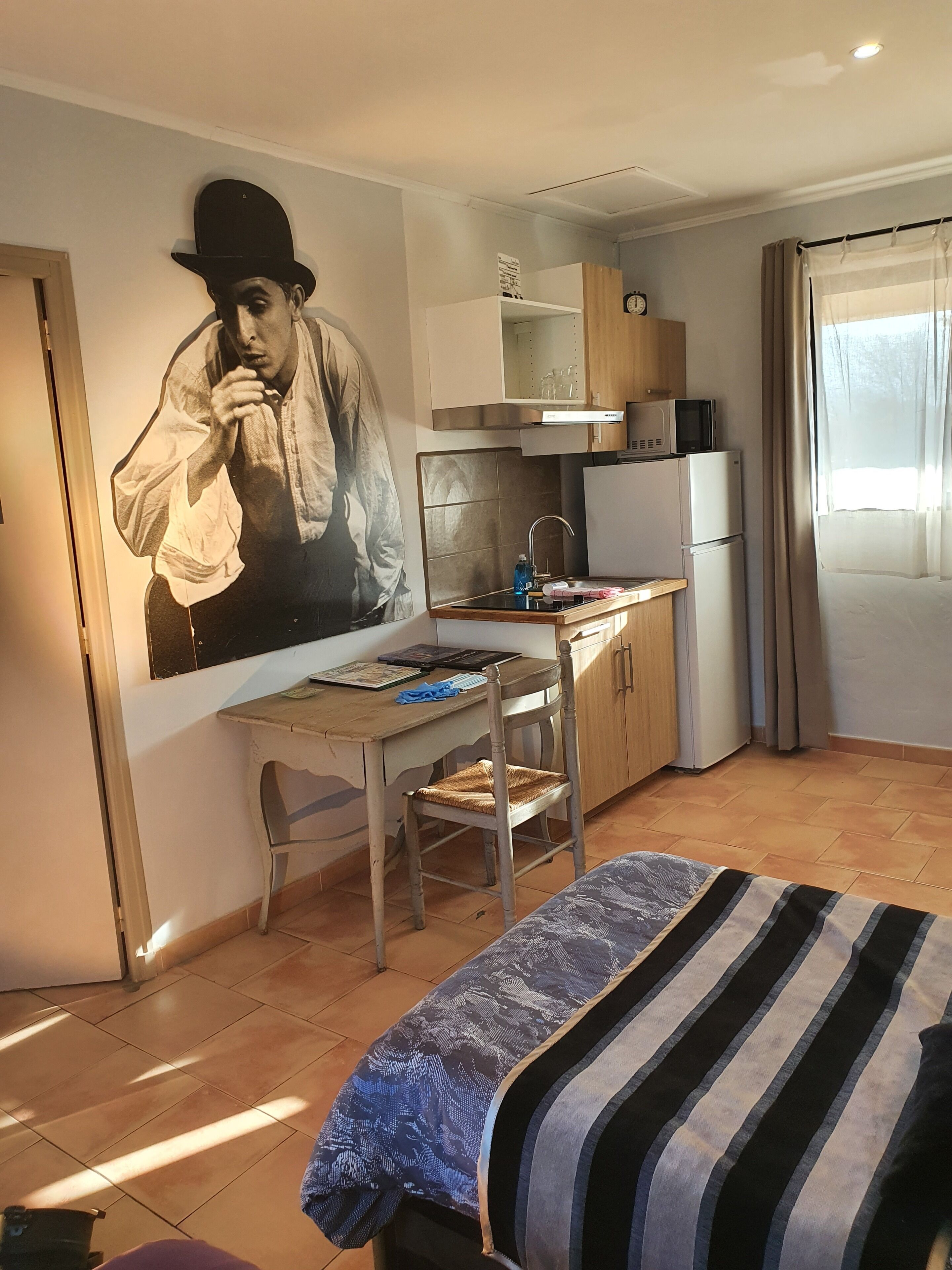Habitación compacta con cama, escritorio y silla, kitchenette y un amplio mural en la pared.
