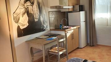 Habitación compacta con cama, escritorio y silla, kitchenette y un amplio mural en la pared.