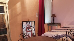Un dormitorio con cama, una mesita con dos sillas, una mesita de noche, aire acondicionado de pared y una ventana con cortinas.