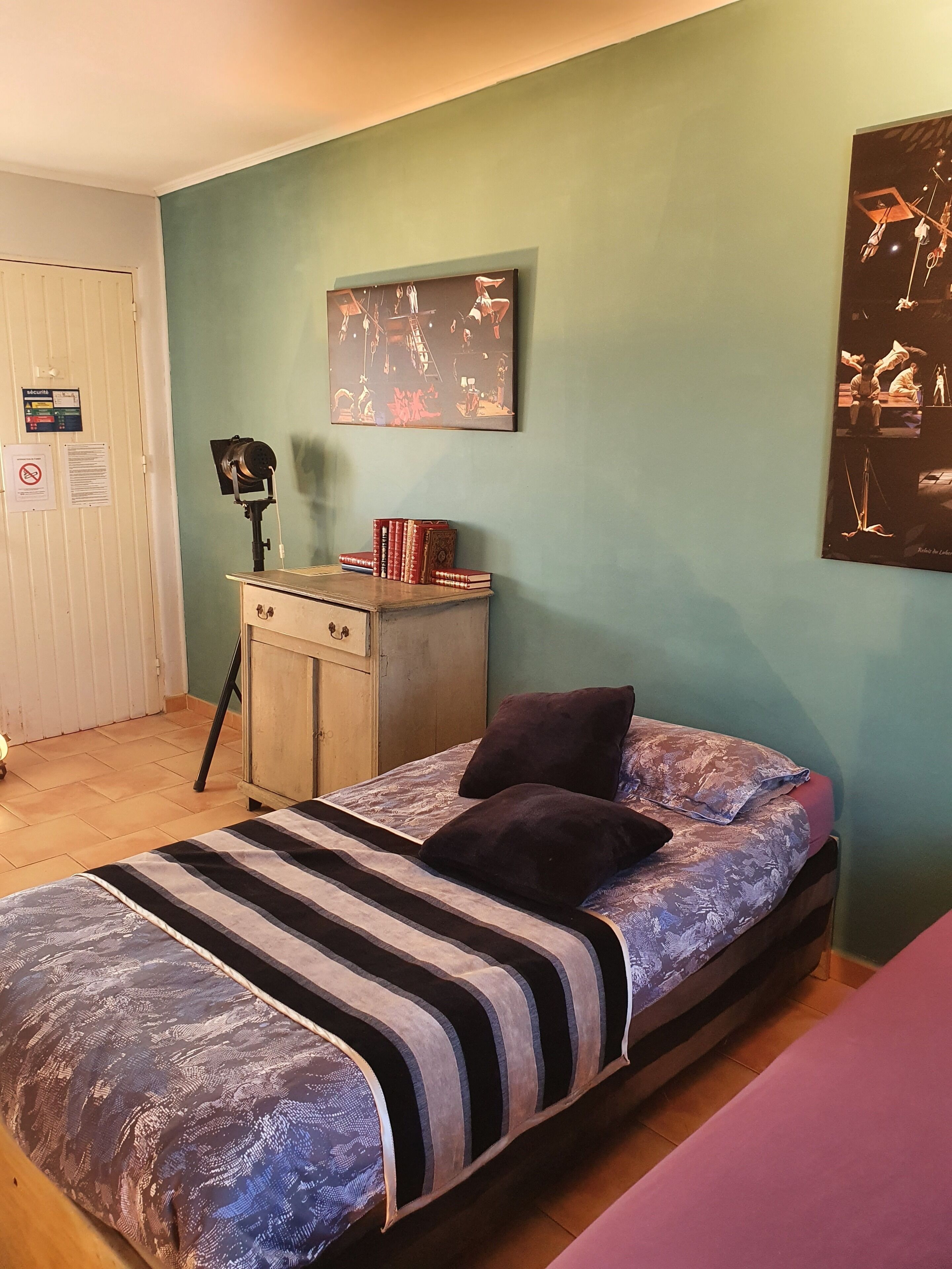 Een slaapkamer met een bed, een dressoir, een aan de muur hangend schilderij en een deur met een bordje.