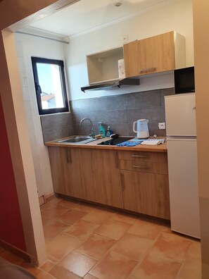 A kitchen with wooden cabinets, a stainless steel sink, a microwave, and a window. - le relais du luberon (Maubec)