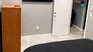 Une chambre à coucher avec un lit, un téléviseur fixé au mur, une armoire en bois et une porte donnant sur une autre pièce.