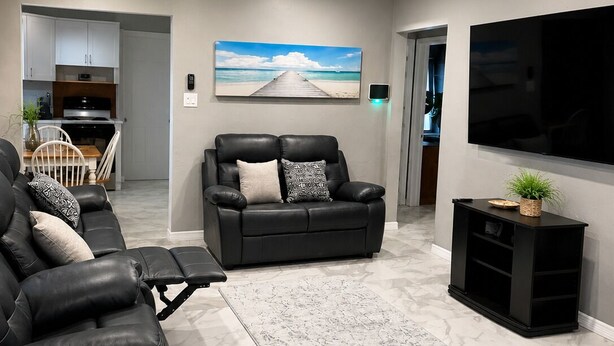 Un salon moderne avec un canapé, un fauteuil inclinable, un téléviseur à écran plat et un ventilateur de plafond.
