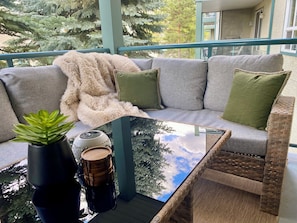 Un balcon avec un canapé, une table en verre, une plante en pot et un objet décoratif.