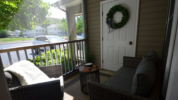 A porch with a wicker sofa, a small round table, and a door with a wreath. - Creekwood Condo Close to Shopping, Dininng and Beaches! (Rehoboth Beach)